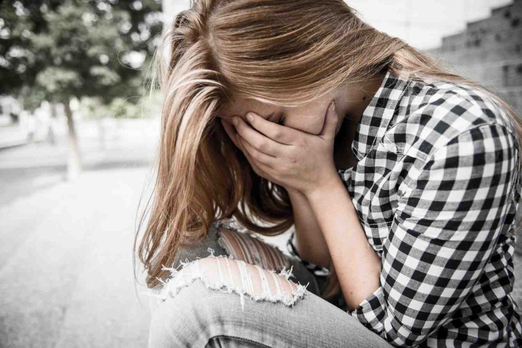 Unhappy depressed teenager with face in hands sitting outdoor